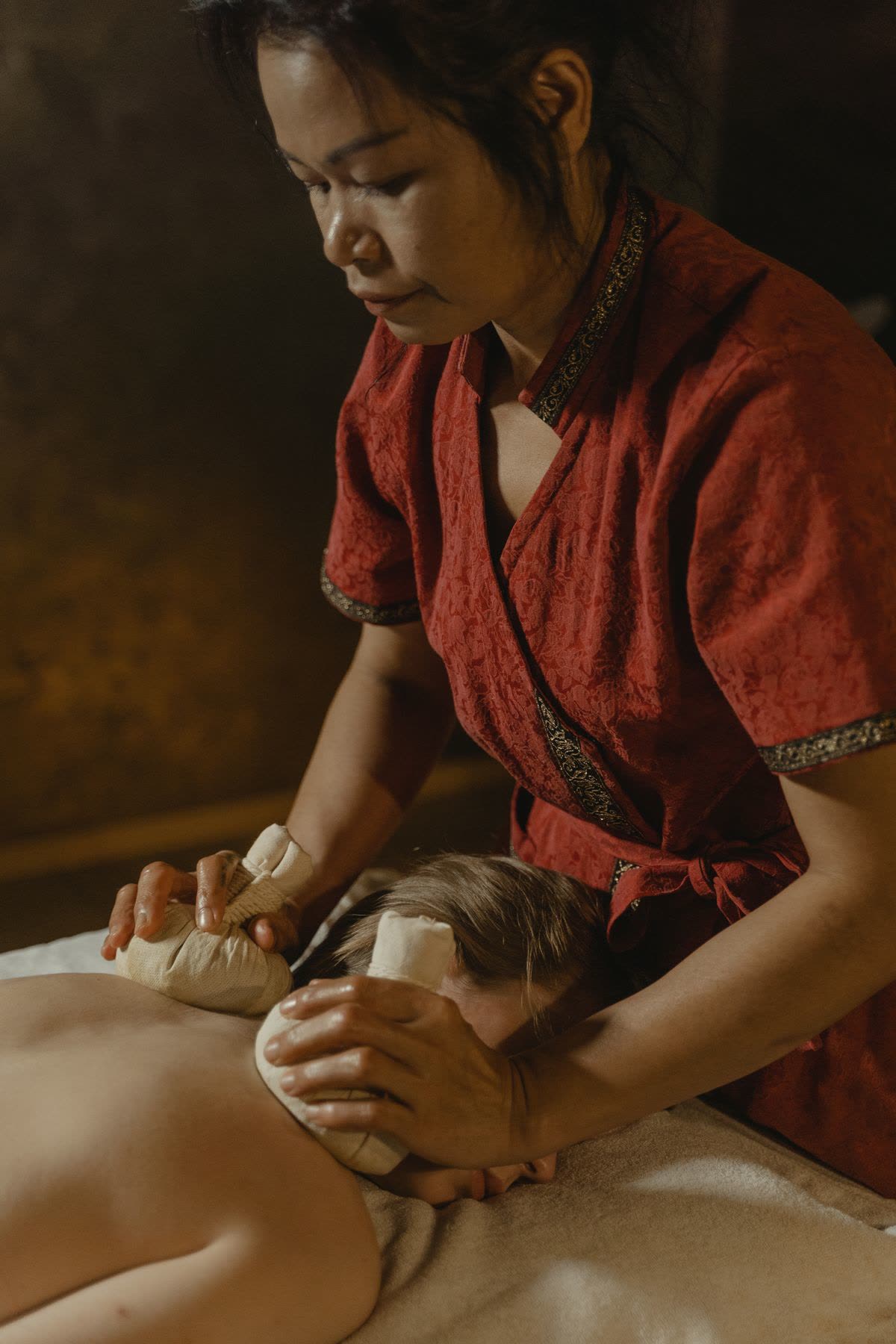 Warm herbal compress balls being pressed on the back during a traditional herbal massage